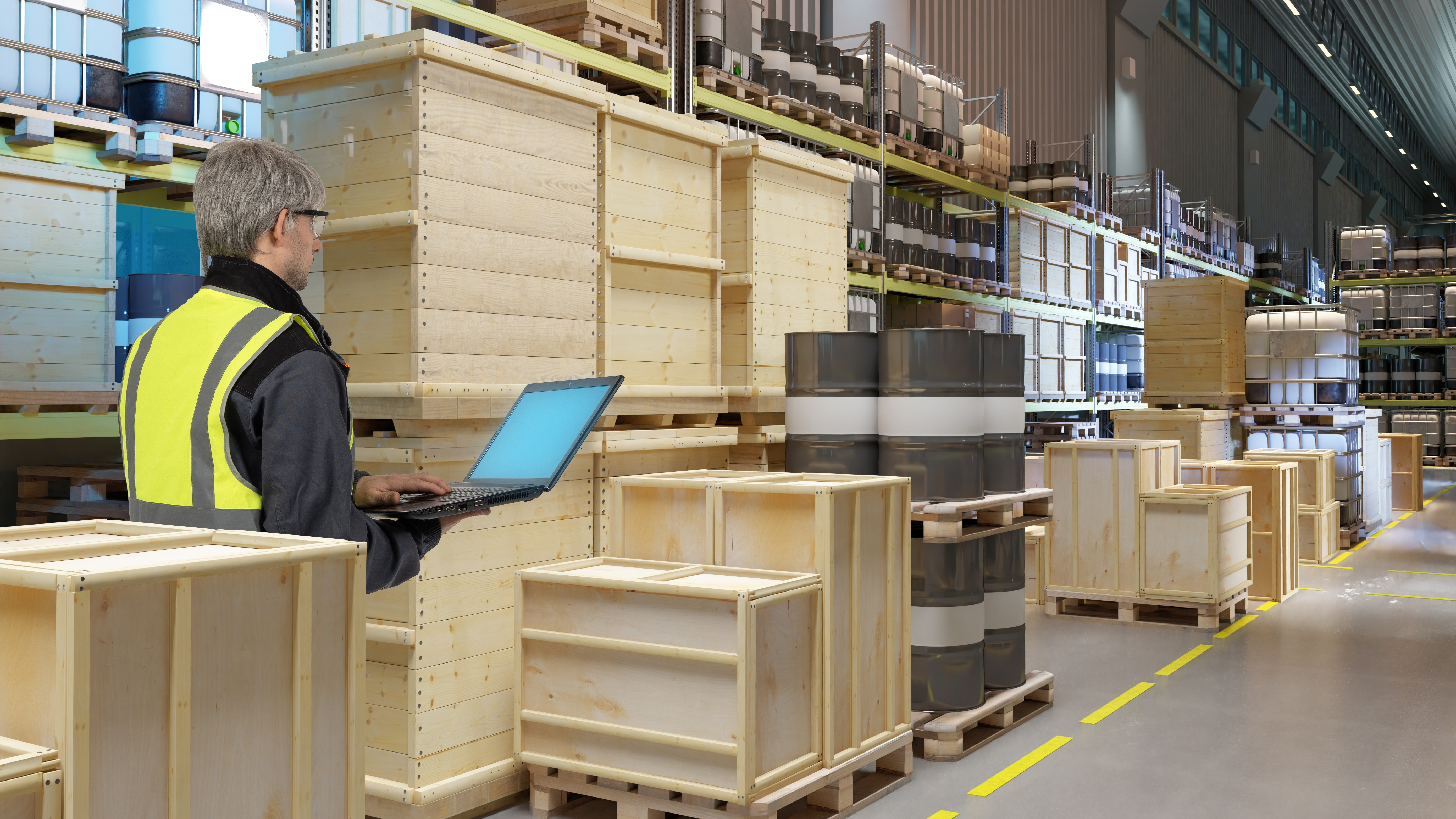 Man warehouse worker with laptop. Manager stands inside storage hangar. Warehouse worker in yellow vest with back to camera. Man logistics center specialist stands among wooden containers.