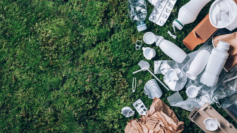 Food plastic packaging, trash on green moss background after picnic in forest.