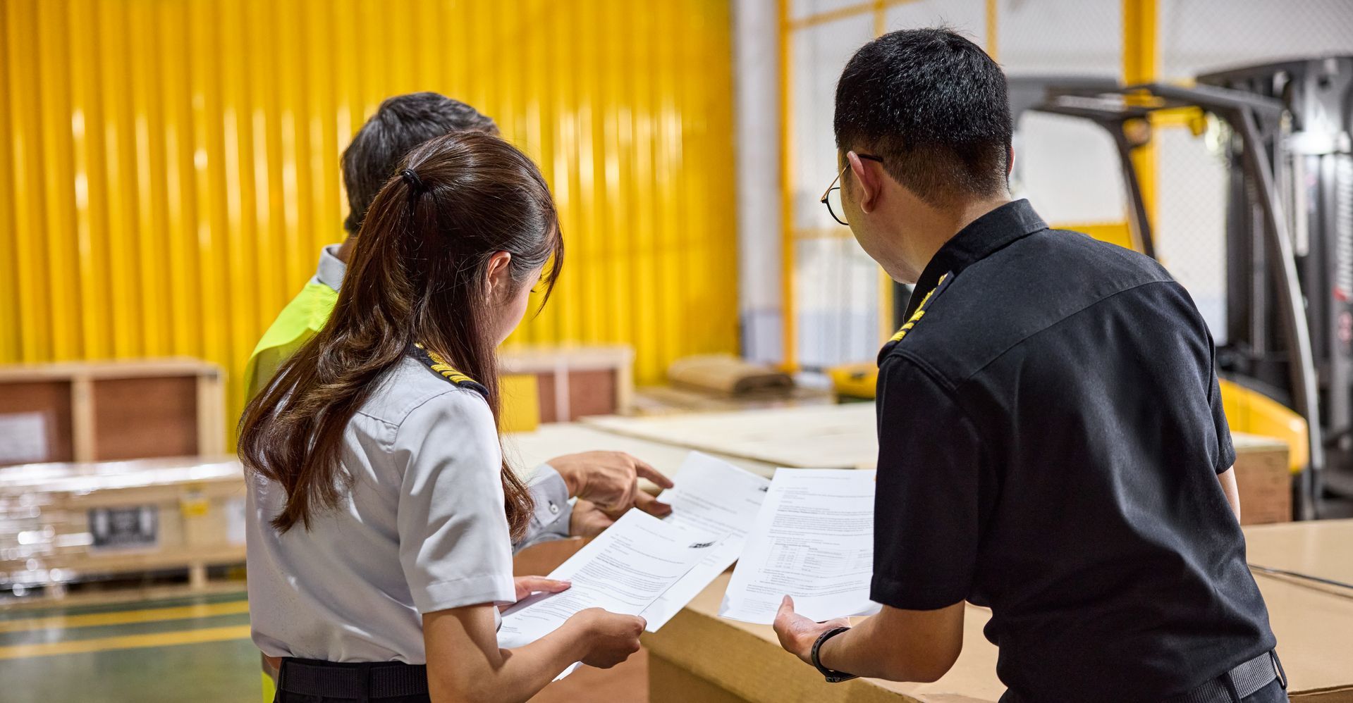 Three customs officers inspect documents for a large transport box.