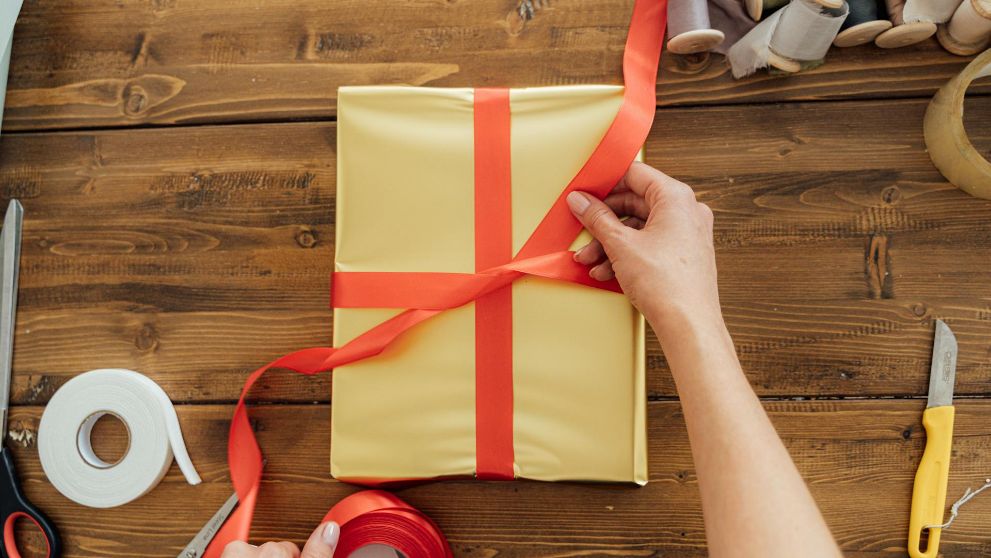 A person tying a red bow on a yellow Valentine’s Day gift box.