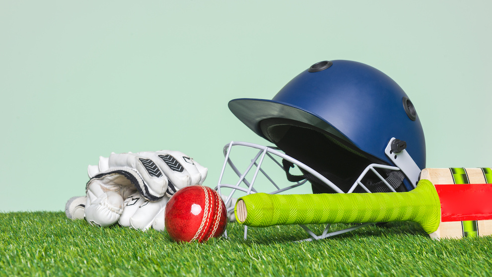 Cricket equipment with bat, ball, helmet and gloves on grass with green background.