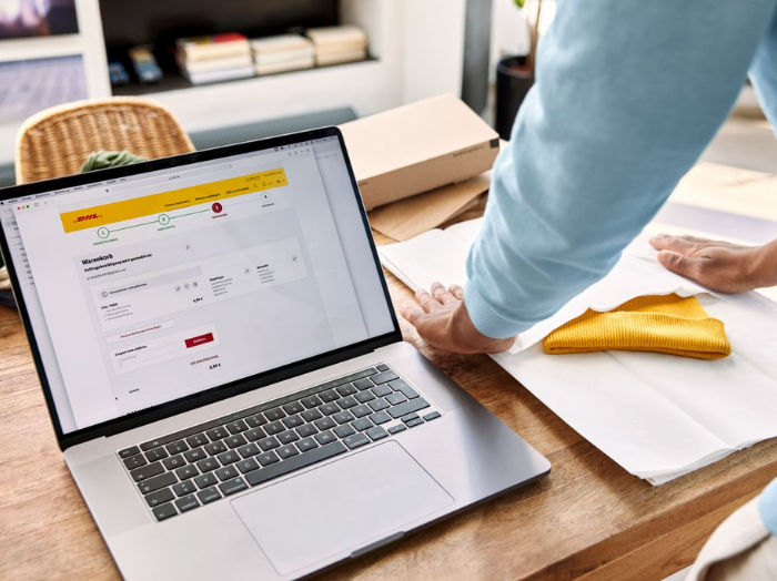 A laptop displaying MyDHL+ and a man packing a yellow beanie.