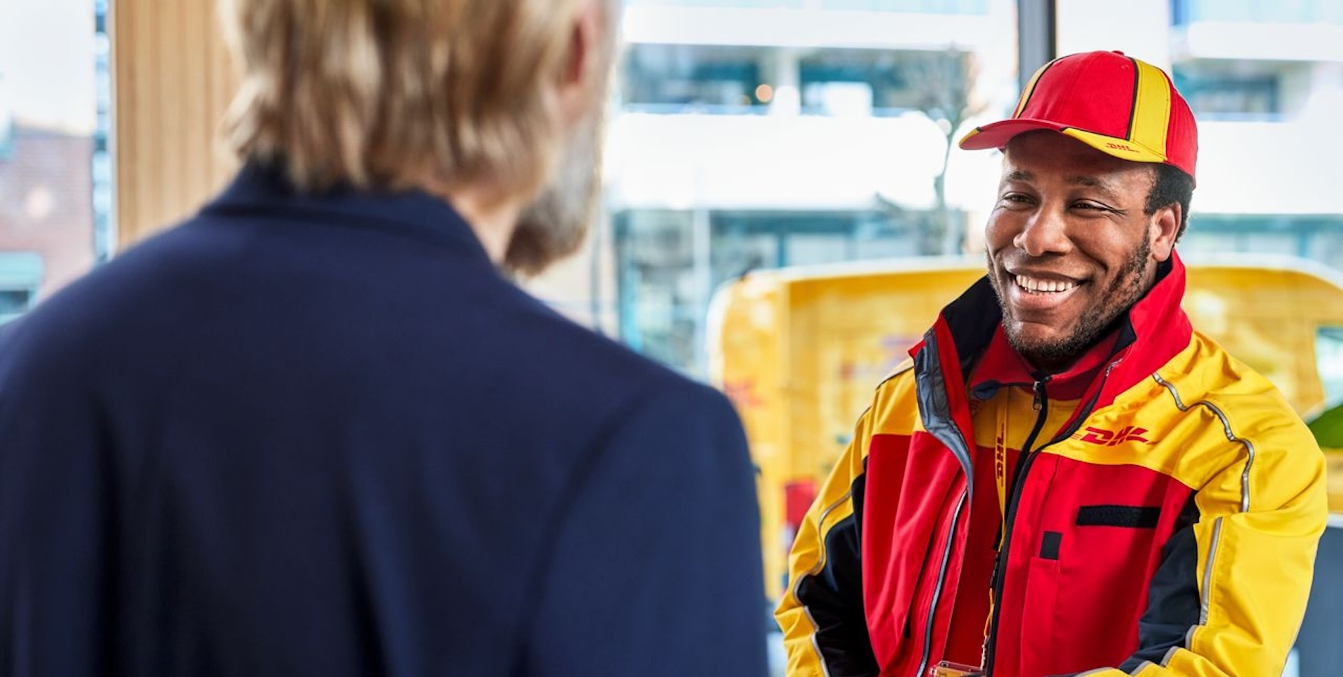 A smiling, male DHL employee is handing a parcel to a male customer