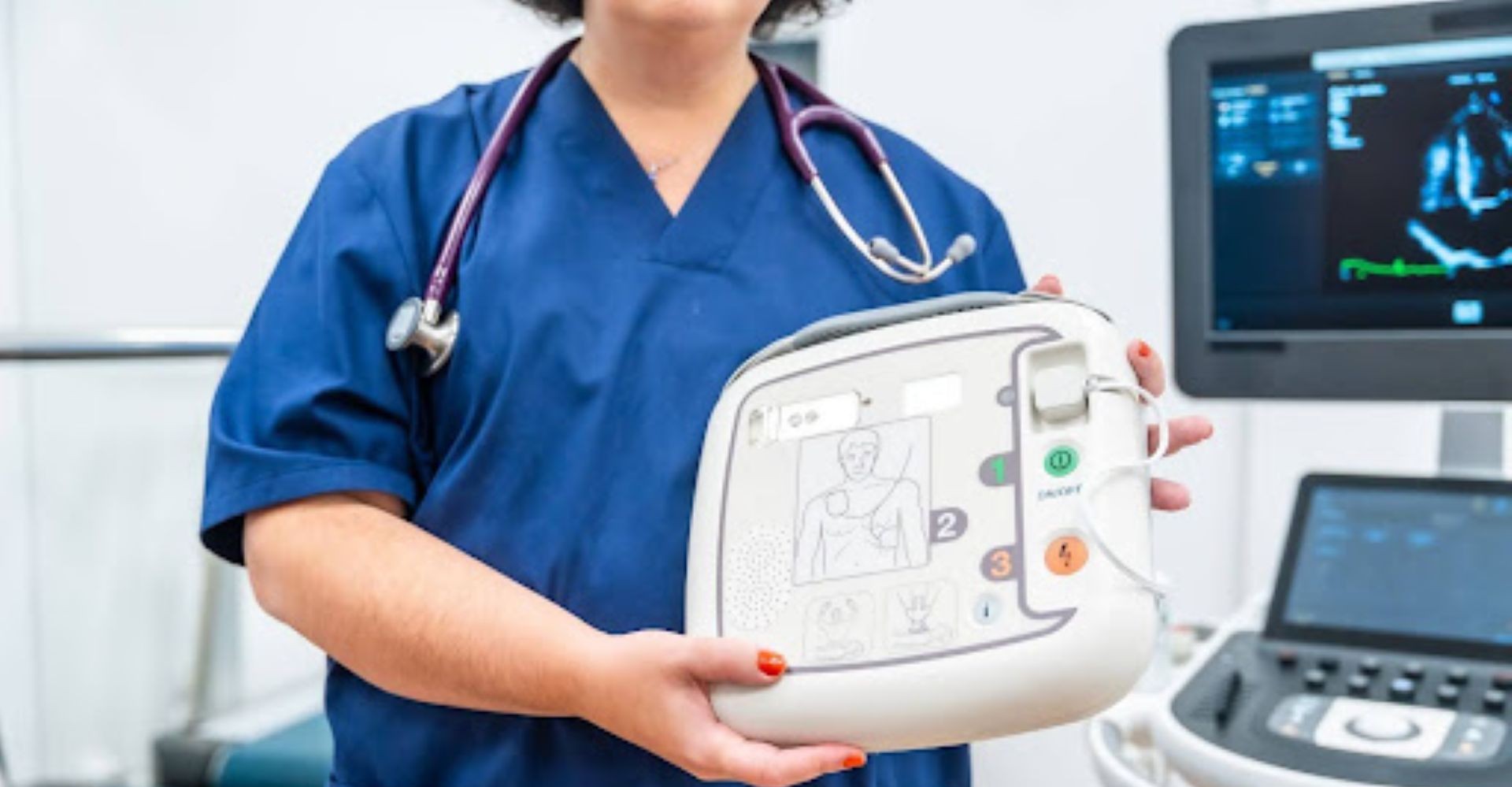 doctor holding a small defibrillator with other medical devices in the background