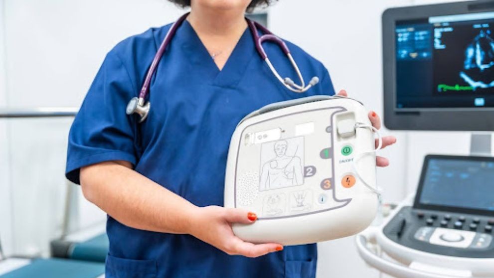 doctor holding a small defibrillator with other medical devices in the background