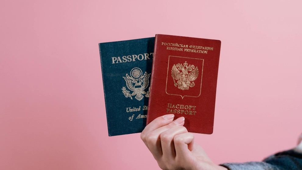 hand holding up two passports on a plain pink background