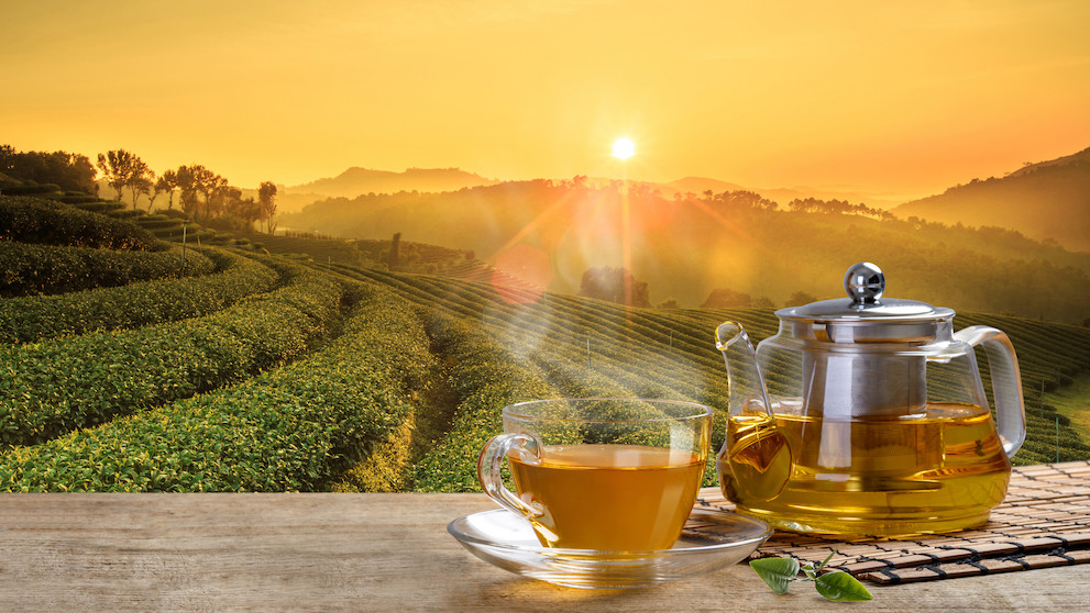 Tea cup and glass jars with leaf on the wooden table in the tea plantations background; Shutterstock ID 671131873; Purchase Order: -
