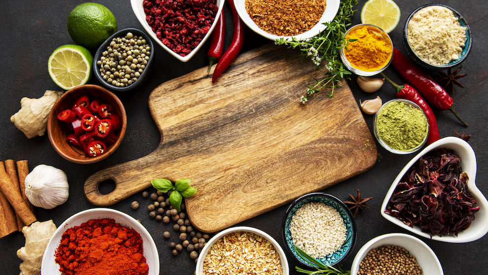 Various spices in a bowls and empty cutting board on black concrete background. Top view copy space.