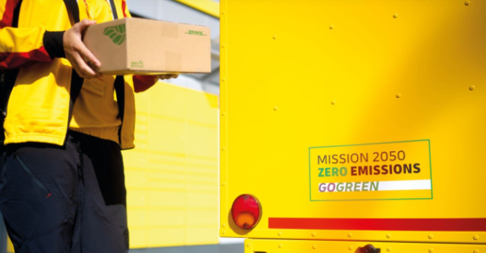 dhl express employee holding a sustainable package next to a gogreen vehicle