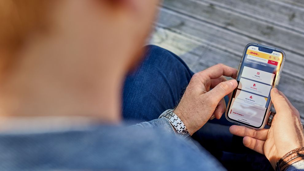 ชายหนุ่มใช้โทรศัพท์เพื่อเรียนดูวิธีชําระเงินออนไลน์ด้วย DHL MyBill