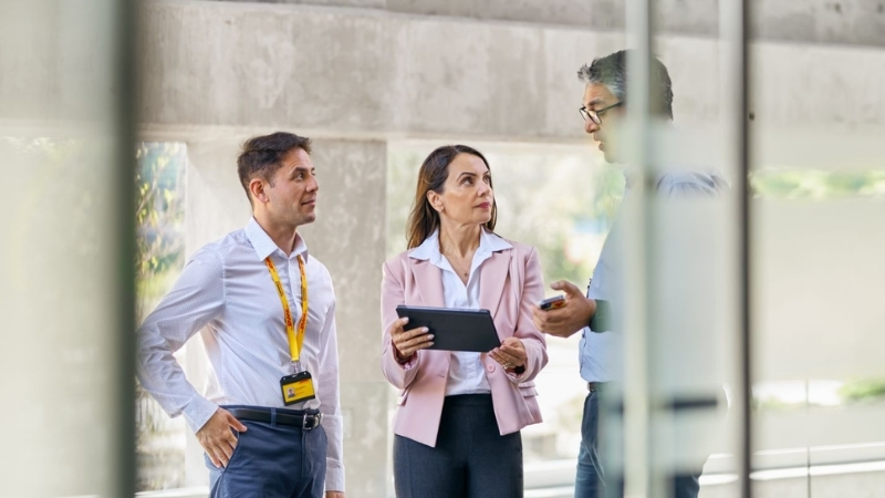 Bir kadın DHL çalışanı, tablet takan iki erkek meslektaşına bir konuyu tanıtıyor.