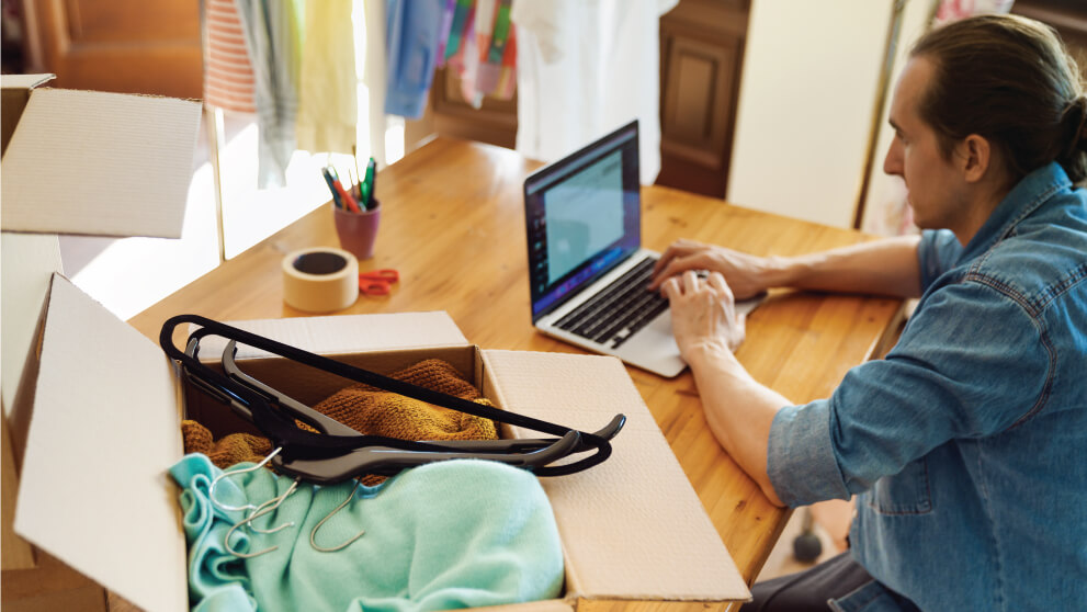 man on his laptop with an open box of clothes next to him