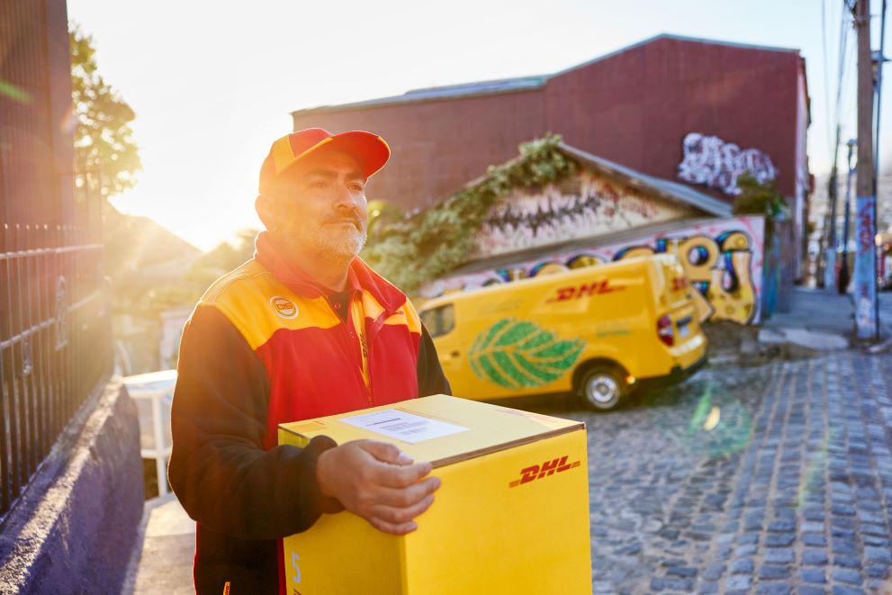 DHL male courier carrying a box against the sunset