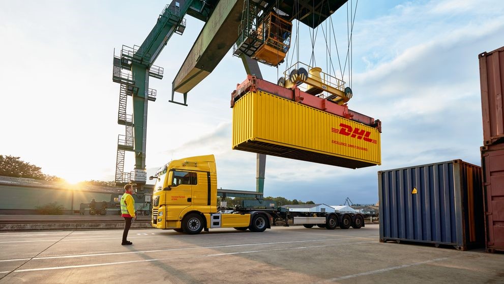 a dhl employee standing in front of a dhl truck while watching a container crane lifting the container
