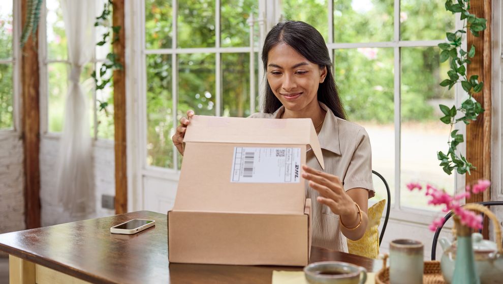 A female customer sits at a table at home and opens her DHL parcel.
