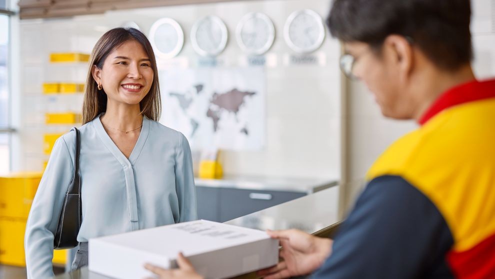 A male DHL employee hands a parcel to a female customer.