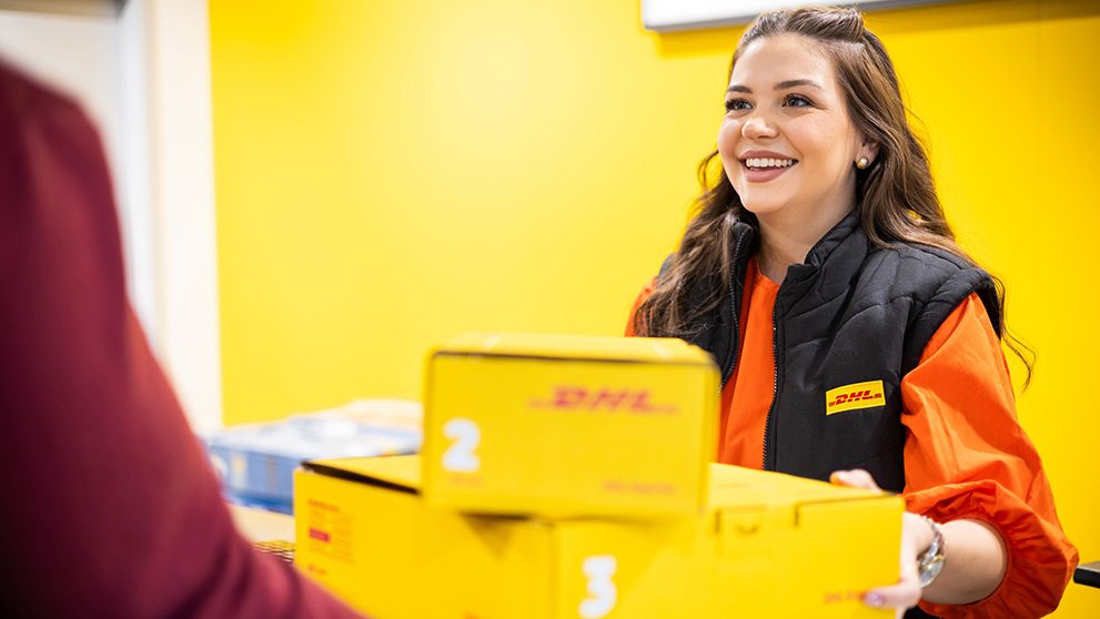 DHL Mitarbeiterin lächelt und nimmt DHL Packete entgegen