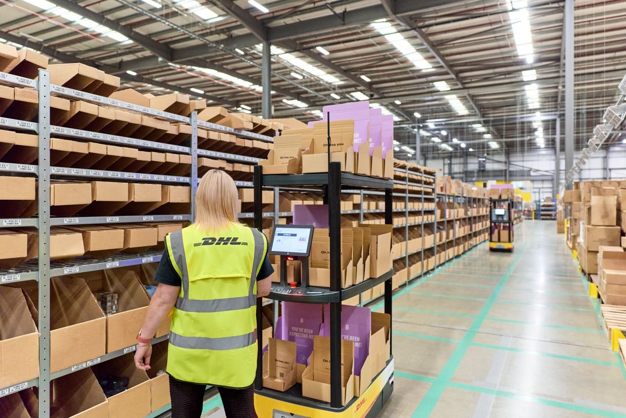 image of warehouse interior with organised shelving units stocked with packages goods and a DHL employee checking inventory