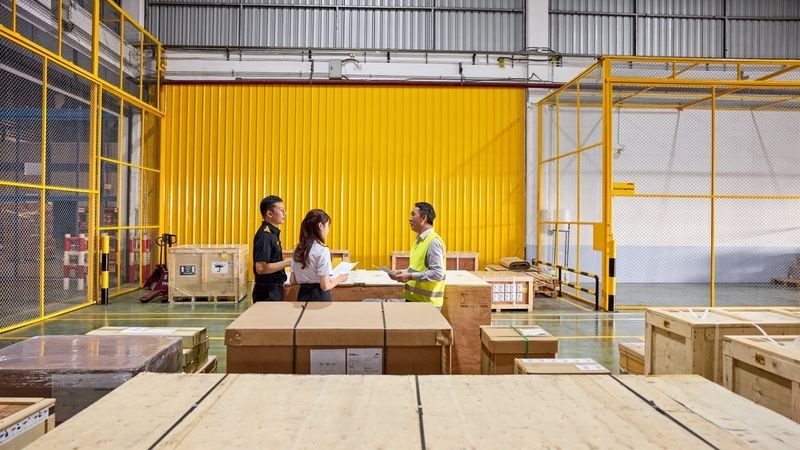 a male dhl expert inspects documents for a large transport box in a multimodal hub together with two customs officers