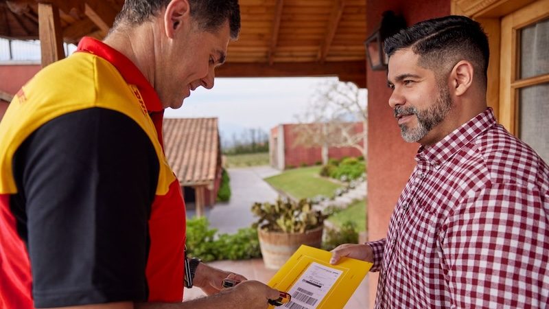 A male DHL employee scanning an express envelope he delivers to a private customer on a vineyard.